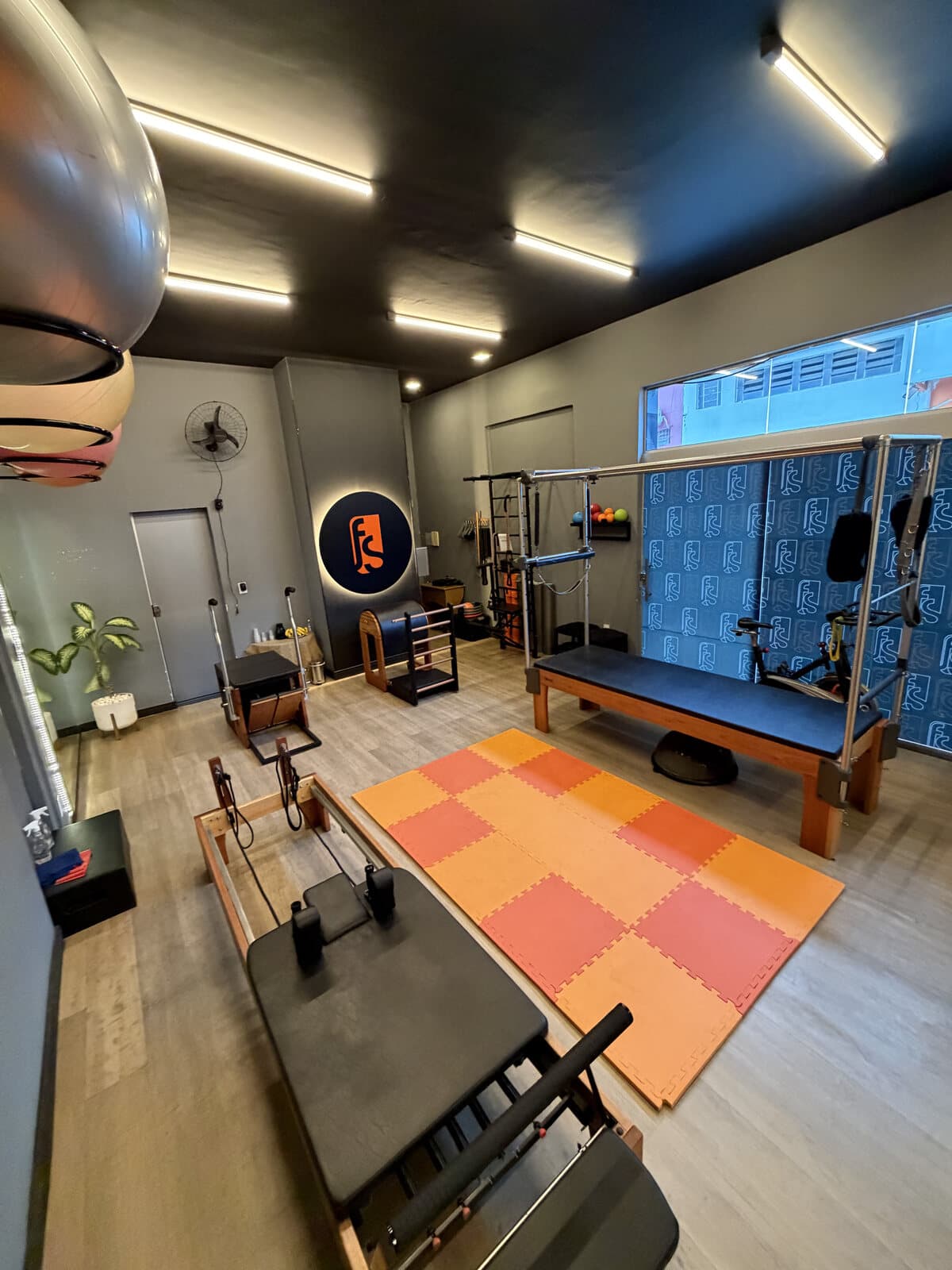 Sala de Pilates da FS Studio, com reformers de madeira, tatames laranja e o logo circular retroiluminado na parede.
